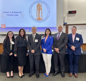 Six people stand side by side in a classroom, dressed in business attire. Behind them, a projector screen displays "Panel 3: Future of Condo Law" with the University of Florida Levin College of Law logo. Notably present is Attorney Barry Ansbacher at the Public Policy Symposium organized by the UF Journal of Law.